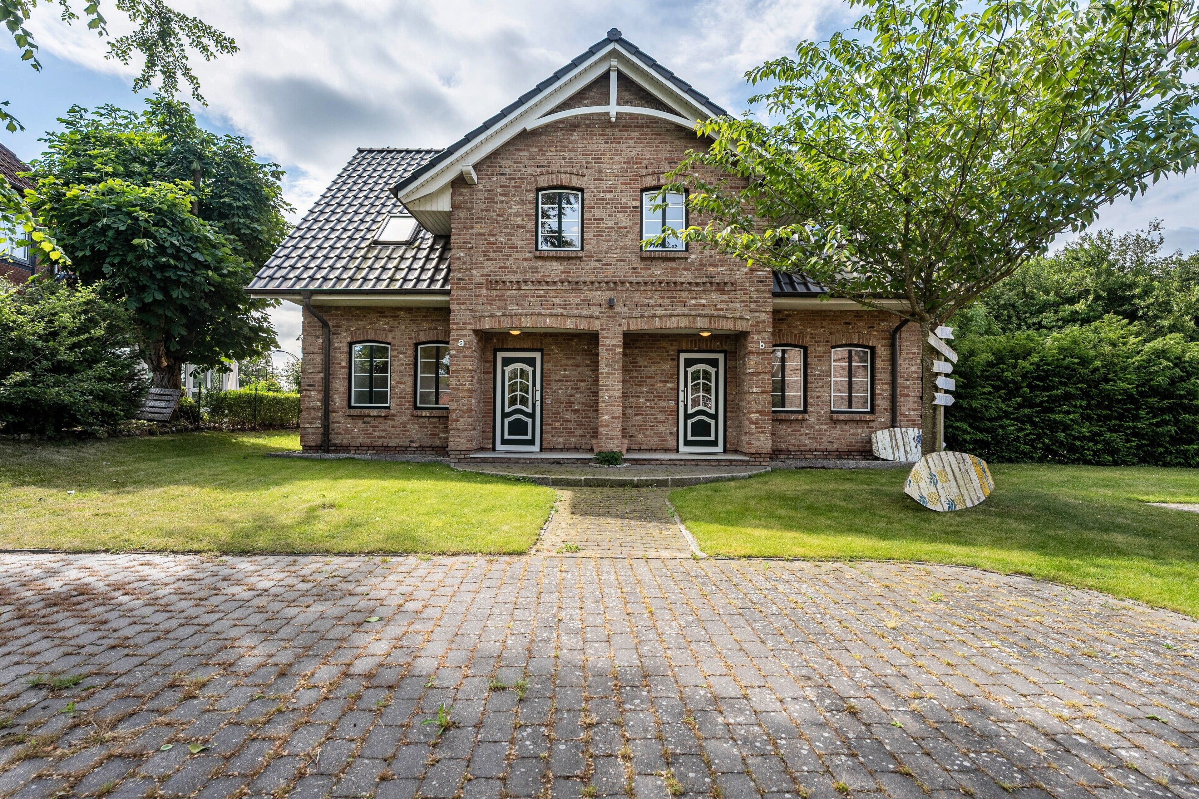 A two-story brick house with a tiled roof, a front entrance with a door, and a paved driveway.