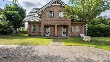 A two-story brick house with a tiled roof, a front entrance with a door, and a paved driveway.