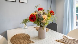 Ein Esstisch mit Blumen in einer Vase, einer gewebten Tischmatte und gerahmten Bildern an der Wand.