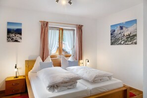 Une chambre à coucher avec un lit en bois, deux tables de chevet, une commode, une fenêtre avec des rideaux et deux tableaux accrochés au mur.