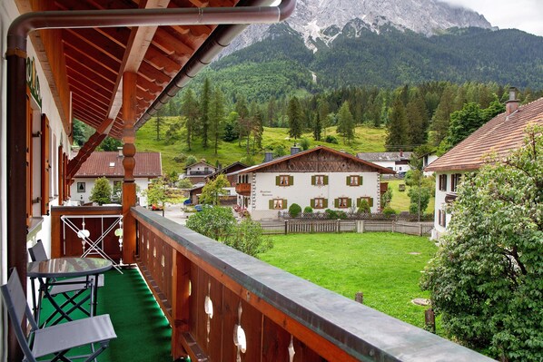 Un balcon donnant sur une montagne, une clôture en bois et un bâtiment à la façade blanche.