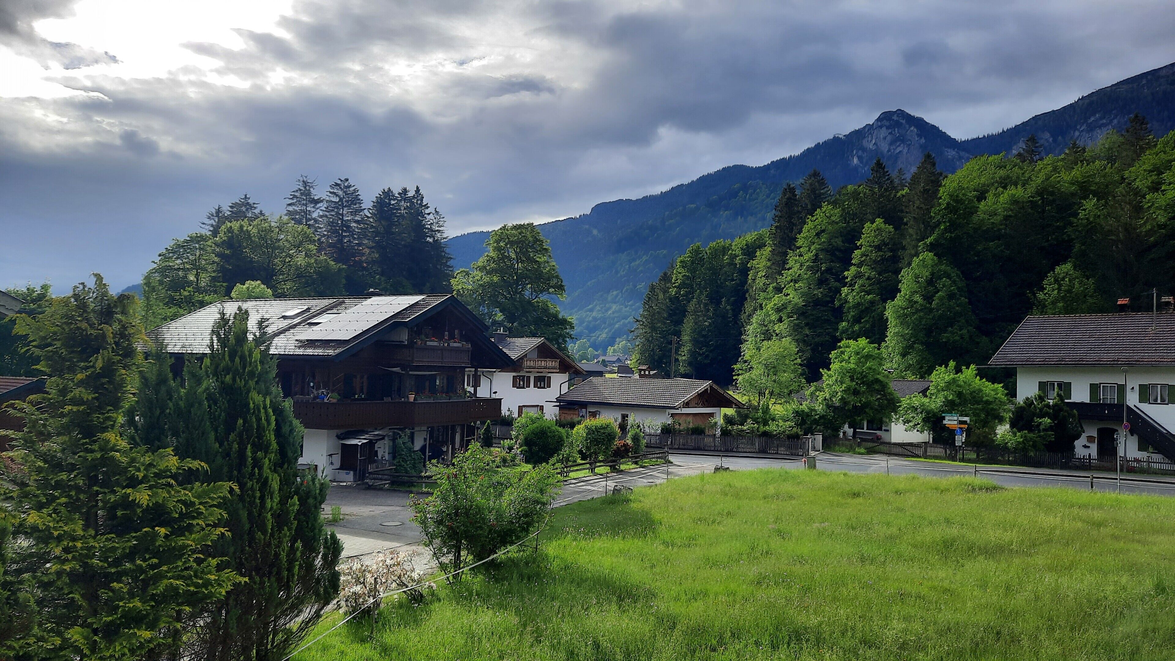 Ein ländliches Dorf mit traditionellen Holzhäusern, einer asphaltierten Straße und Bergen im Hintergrund.
