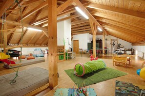 A spacious attic room with wooden beams, a play area with a green tunnel, and a wooden table.