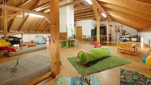 Una habitación amplia en el ático con vigas de madera, una zona de juegos con un túnel verde y una mesa de madera.