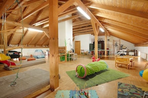 Une vaste pièce mansardée avec des poutres en bois, un espace de jeux doté d’un tunnel vert et une table en bois.