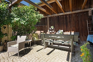 A wooden pergola with a bench and chairs, a wooden fence, and a table with a blue checkered tablecloth.