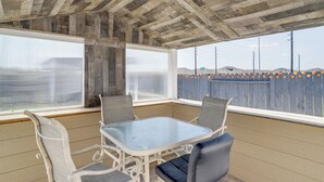 Een overdekt terras met een tafel en stoelen, grote ramen en uitzicht op een hek met oranje decoraties.