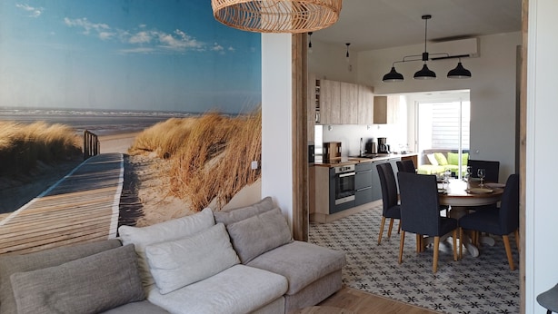 A modern living room with a large wall mural of a beach, a grey sofa, and a woven light fixture.
