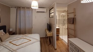 A modern bedroom with a bed, bedside table, and a TV. There is a shower area with a glass door and a towel rack.