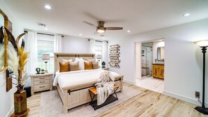 A bedroom with a large bed, bedside tables, a nightstand, a floor lamp, a ceiling fan, and a view into the bathroom. - 'Peace & Tranquility': Home 2 Mi to Dtwn Tulsa! (Tulsa)