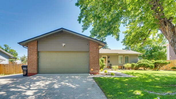 Une maison de plain-pied avec un garage, une cour avant avec une pelouse et un arbre, et une clôture en bois.