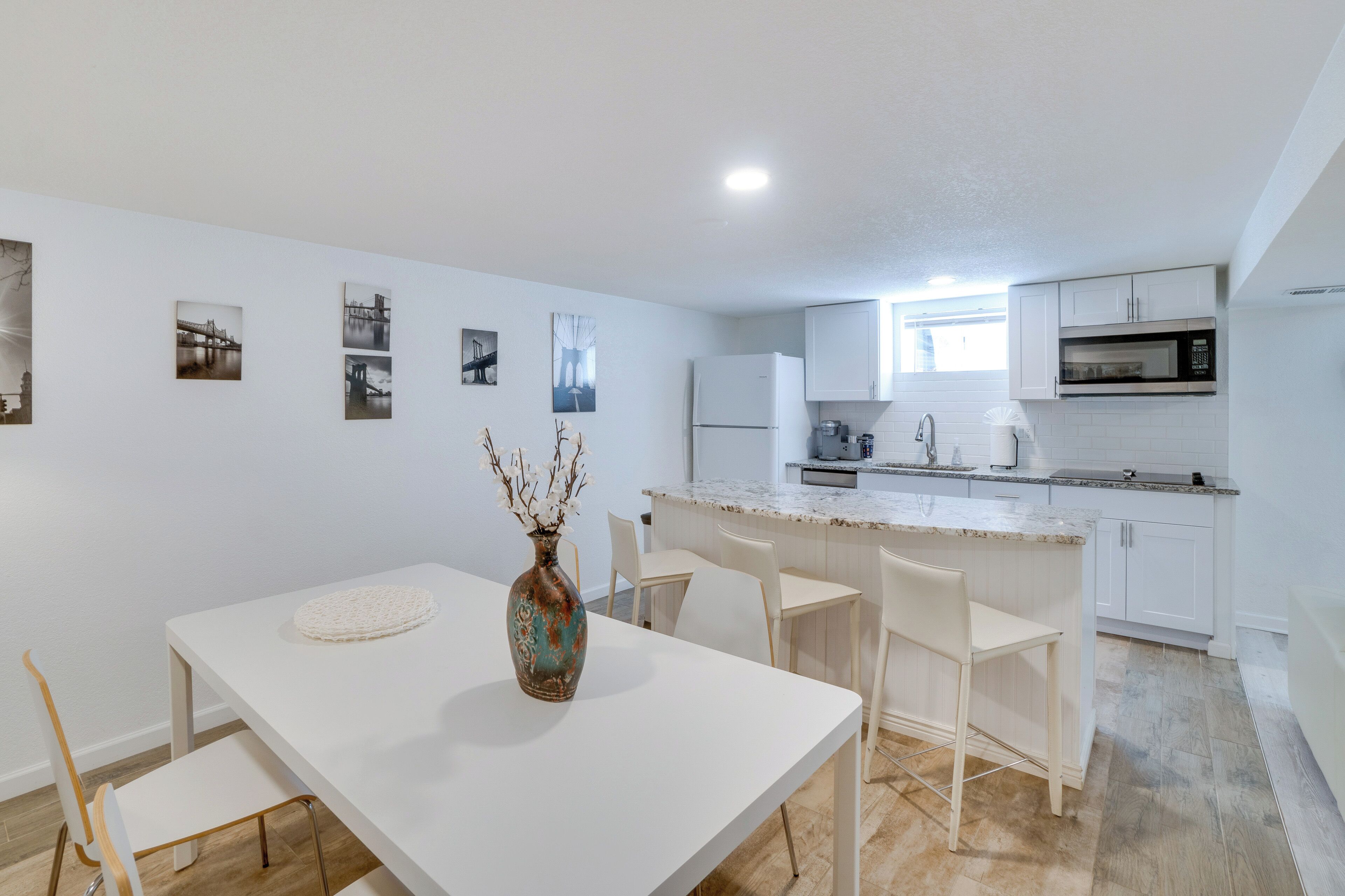 Uma cozinha moderna com armários brancos, micro-ondas embutido e um espaço de refeições com mesa e cadeiras brancas.
