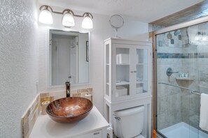 Un bagno con box doccia in vetro, un water bianco, un lavabo con lavandino in vetro e un mobile con ante in vetro.