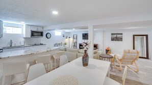 Une cuisine moderne équipée d’un four à micro-ondes, d’une horloge et d’un coin repas avec une table et des chaises blanches.