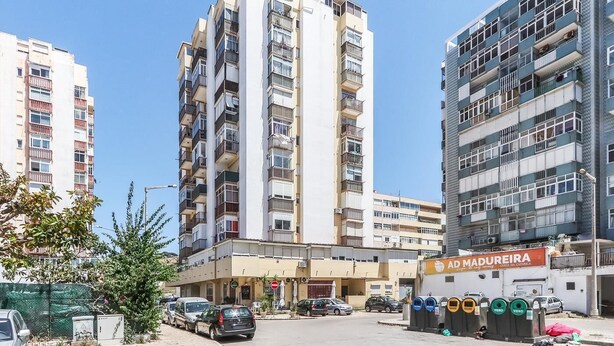 Un edificio residencial de varios pisos con balcones, un estacionamiento y una tienda con un letrero que dice "AD MADUREIRA".