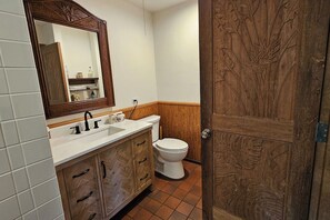 A bathroom with a wooden vanity, a white sink, and a toilet. - #37 1 Bed/Bath with Ocean View (Naalehu)