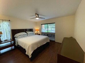 A bedroom with a bed, bedside table, lamp, window with blinds, and a ceiling fan. - #37 1 Bed/Bath with Ocean View (Naalehu)