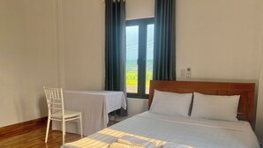 A hotel room with a large bed, a small table, a chair, and a window with a view of greenery. - Happy field homesaty (Phong Nha)