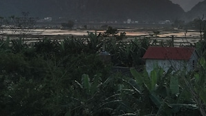A landscape with mountains, a river, and a small building with a red roof. - Happy field homesaty (Phong Nha)