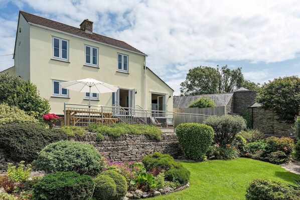 Une maison à deux étages dotée d’un balcon, d’un mur en pierre et d’un jardin bien entretenu.