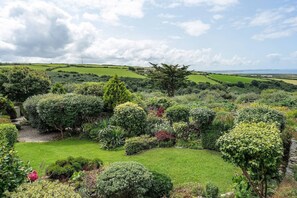 A lush garden with various shrubs and trees, a well-maintained lawn, and a distant view of the sea. - Peaceful Home, Sea Views, Private Parking (Trewarmett)