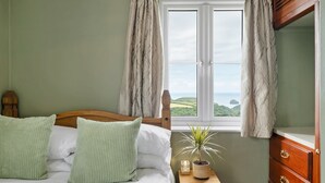 Une chambre à coucher avec un lit, une table de chevet ornée d’une plante, une commode et une fenêtre avec des rideaux.