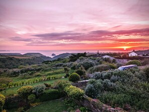 Un paysage côtier avec des collines douces, un coucher de soleil et un petit village composé de maisons et de verdure.