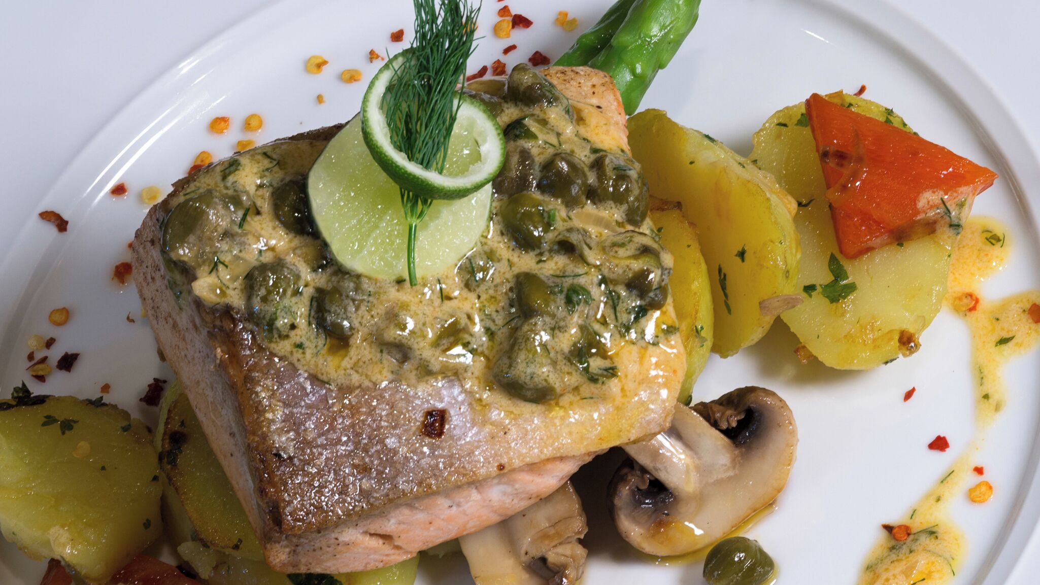 A plate with a piece of meat topped with a creamy sauce, surrounded by roasted vegetables and garnished with herbs.