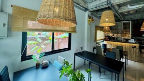 Un intérieur moderne avec un coin repas, de grandes fenêtres et des lampes suspendues en osier.