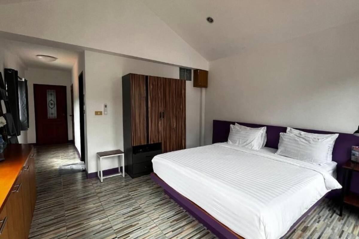 Quarto de hotel moderno com uma cama grande, um guarda-roupa de madeira, uma mesinha e uma escrivaninha com uma luminária.