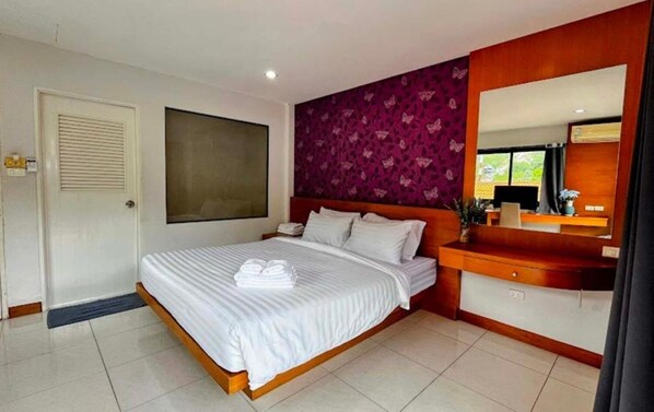 A hotel room with a large bed, a wooden headboard, a vanity with a mirror, and a window with a view of greenery.