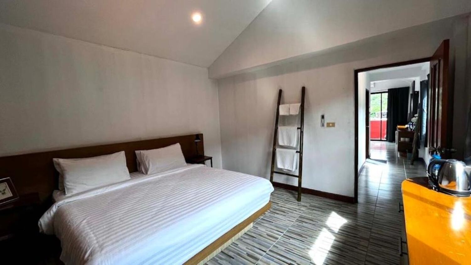 Una camera d'albergo con un letto grande, una testiera in legno, un comodino, uno specchio e un bagno visibile attraverso una porta aperta.