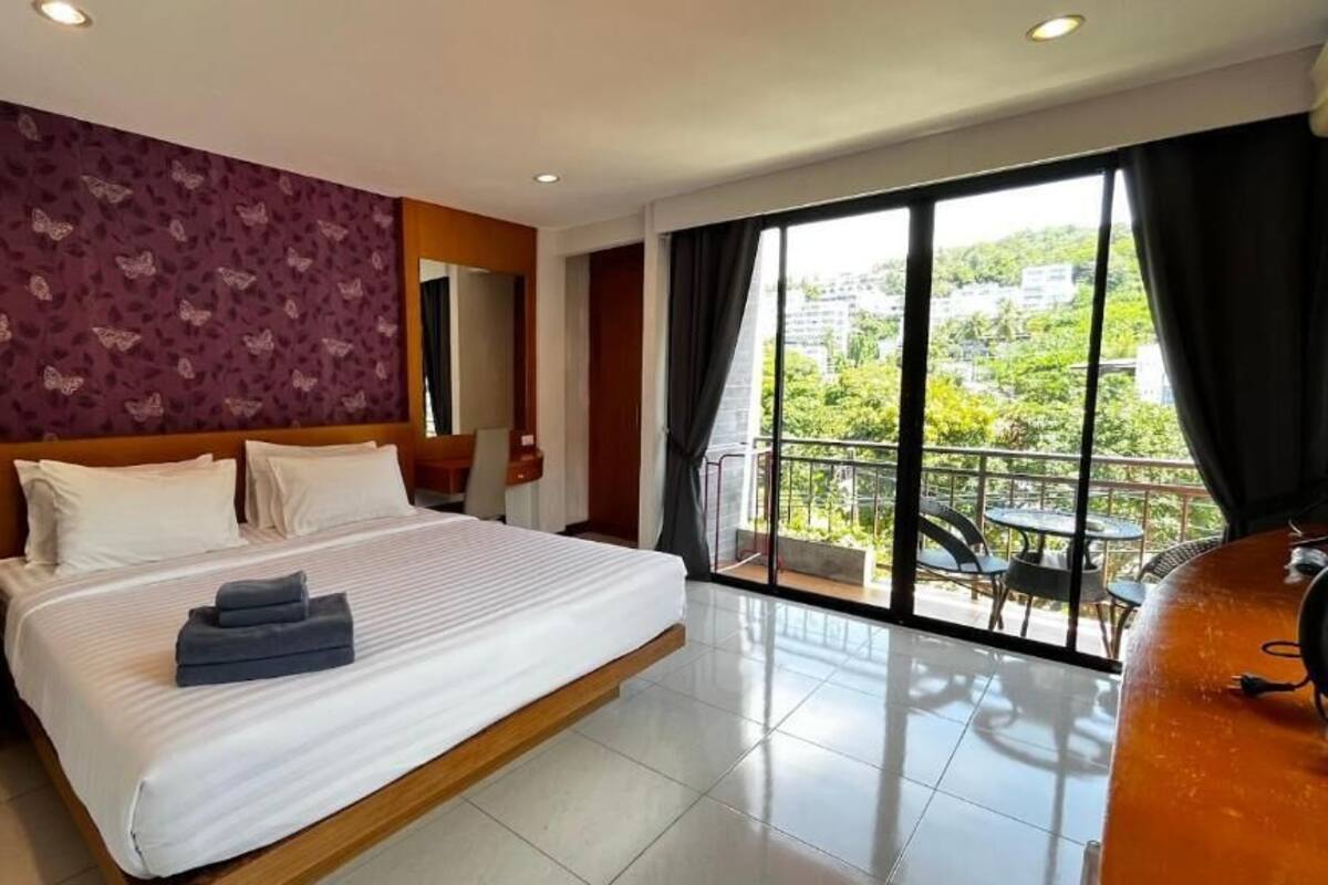 Quarto de hotel com uma cama grande, mesa de cabeceira, espelho e varanda com vista para o verde.
