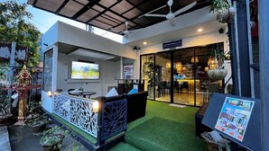 Un espace extérieur moderne, aménagé avec des sièges, une paroi en verre, du gazon synthétique et un ventilateur de plafond.
