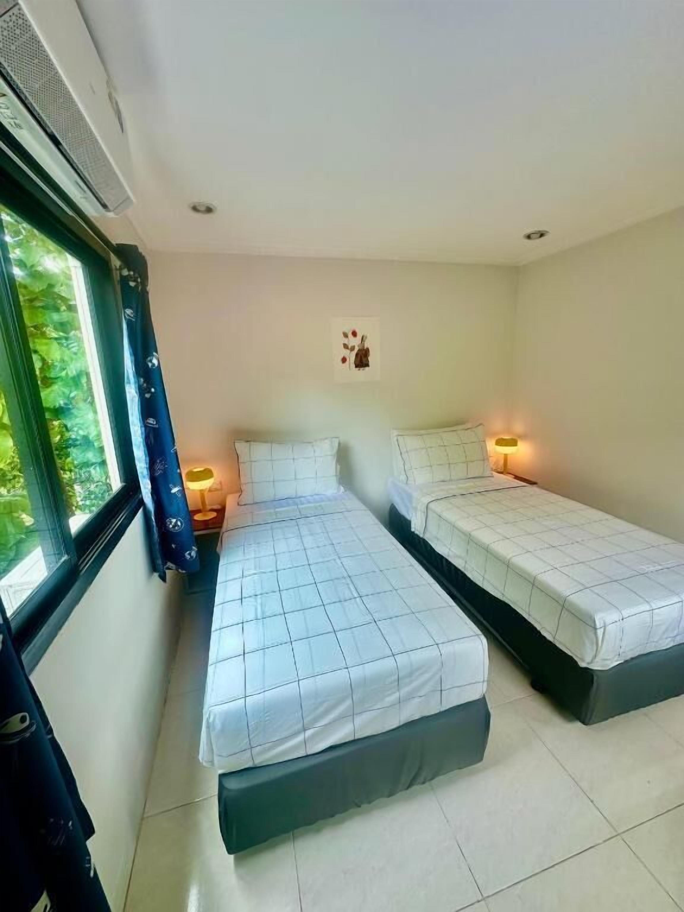 Una habitación con dos camas, una ventana con cortinas, una lámpara de pared y un cuadro pequeño.