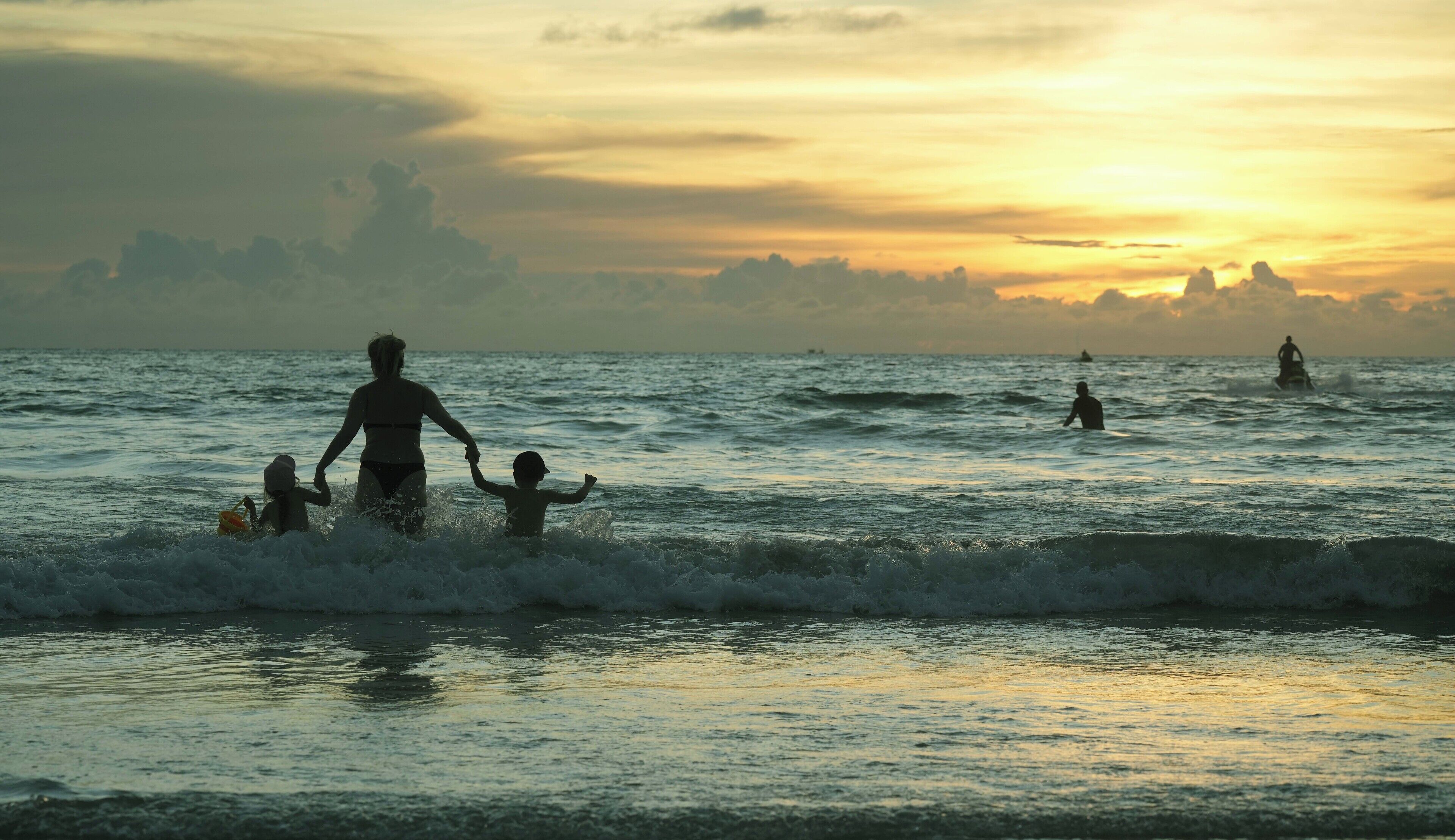 A sunset over the ocean with people in the water.