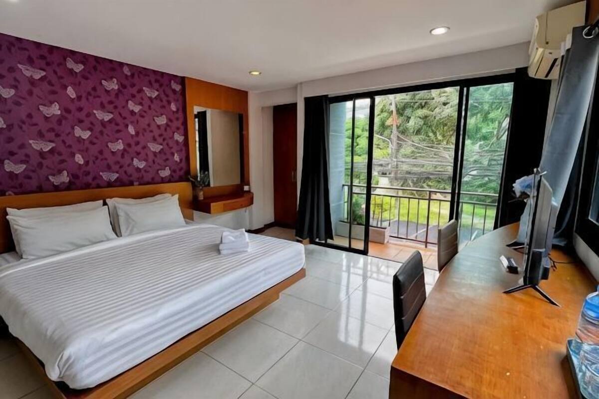 Quarto de hotel com cama grande, escrivaninha, cadeira, varanda e vista para o verde, além de porta de correr de vidro.