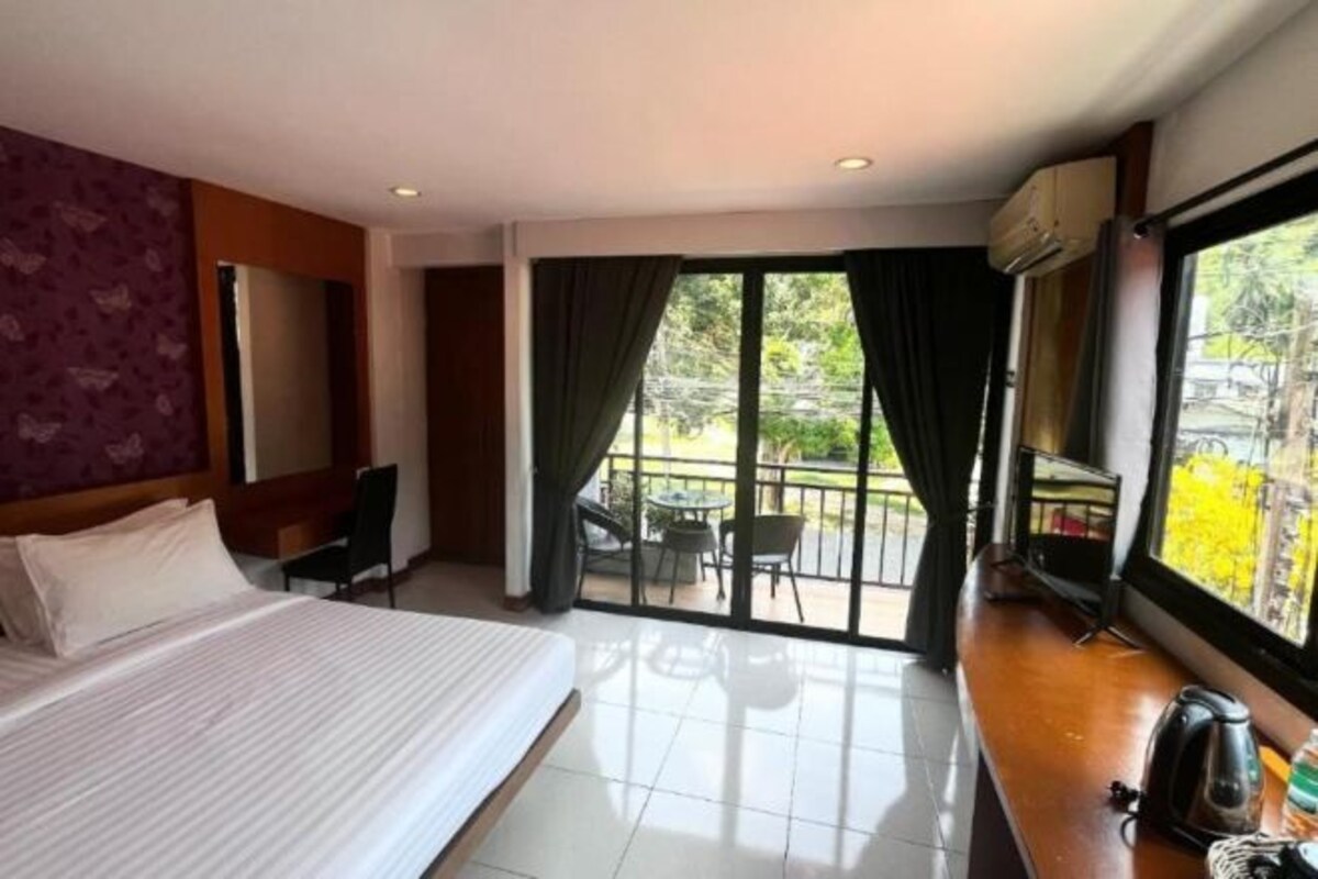 A hotel room with a bed, a desk, a chair, and a balcony with a view of greenery.