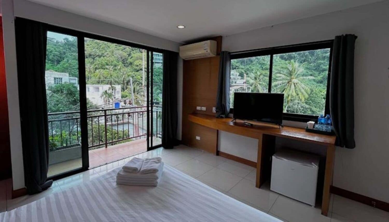 A hotel room with a balcony, a TV, a desk, and a bed with towels.
