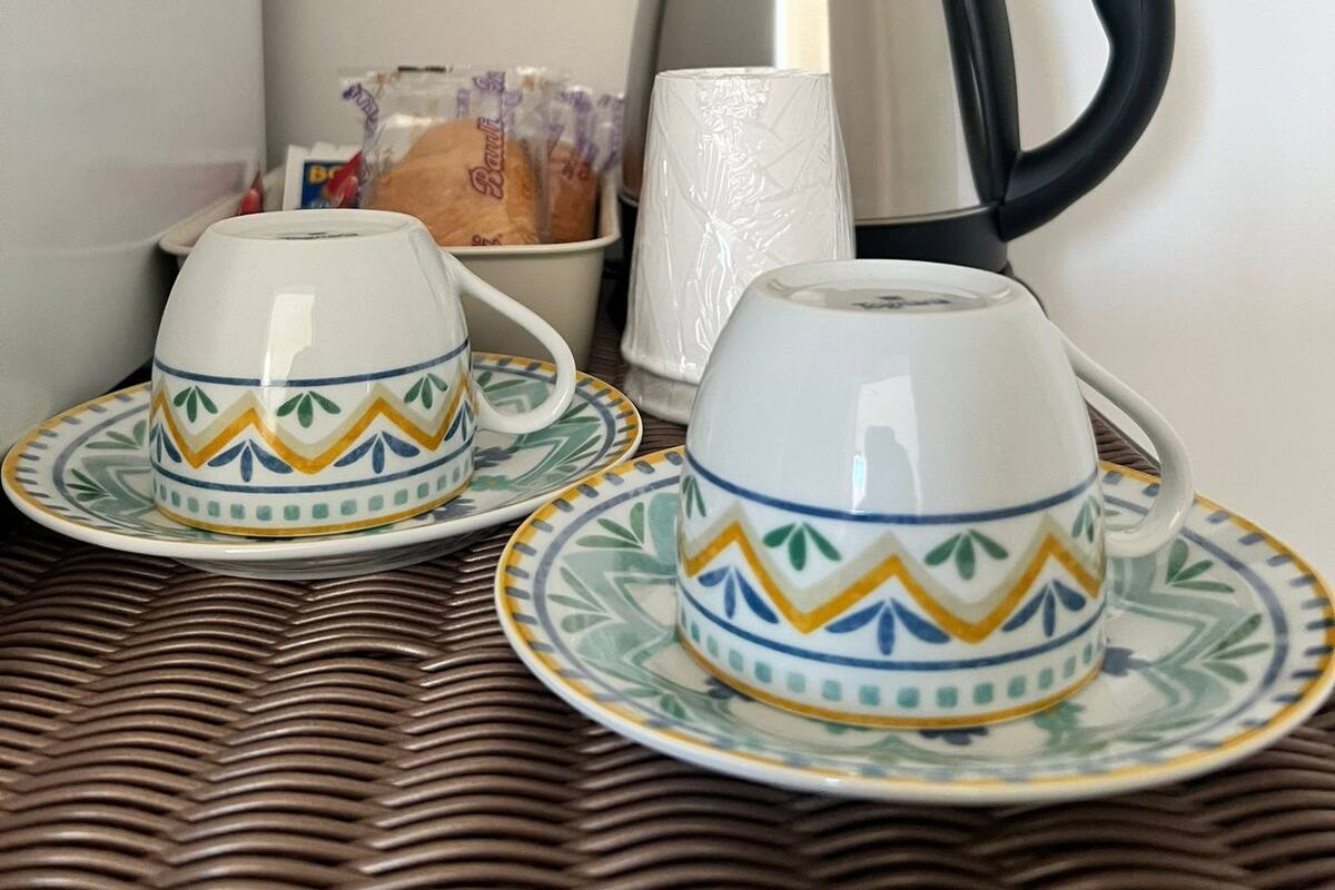 Two white cups with blue and yellow patterns on a woven table.