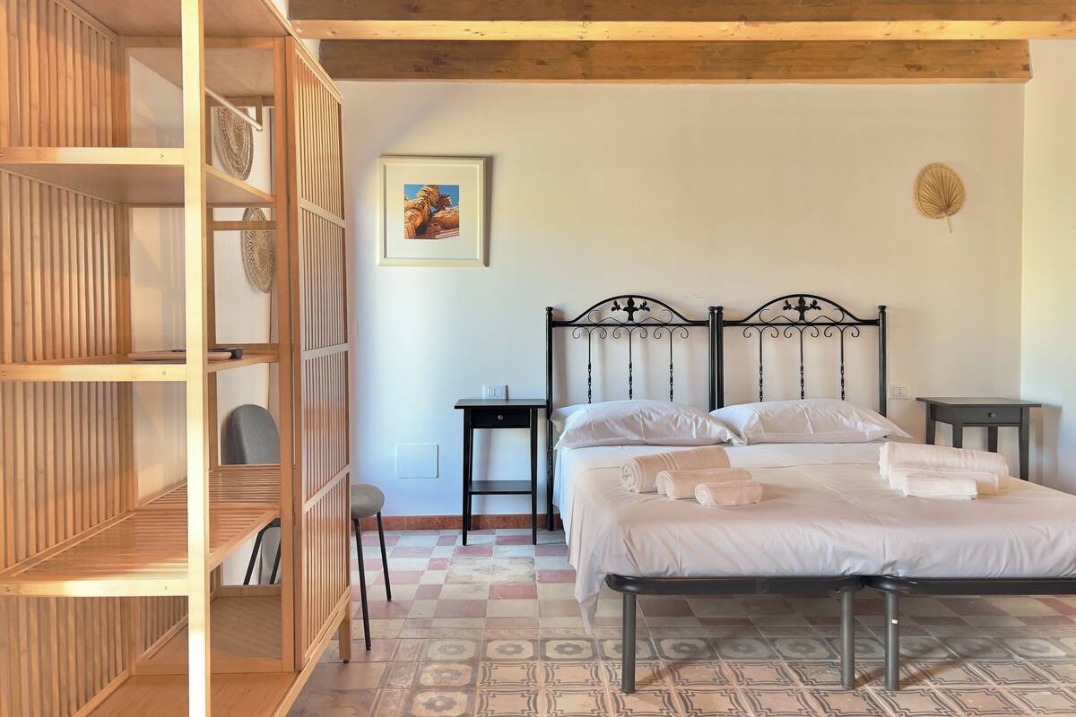 A bedroom with a bed, a wooden wardrobe, a small table, and a chair.