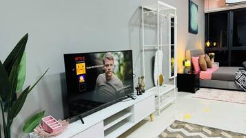 A modern living room with a flat-screen TV, a white entertainment unit, a bed, and a large window.