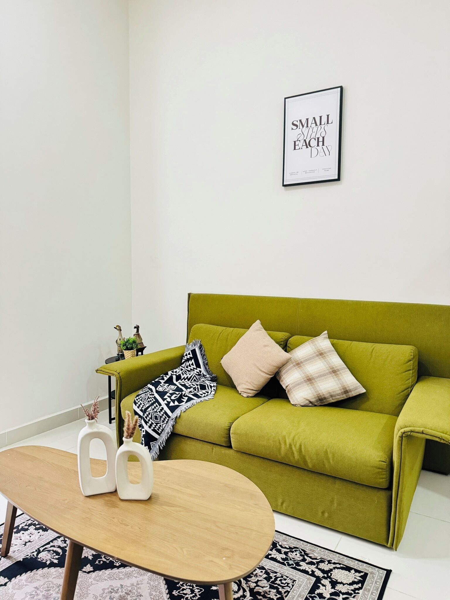 Un salon moderne avec un canapé vert, une petite table ronde et une citation inspirante encadrée accrochée au mur.