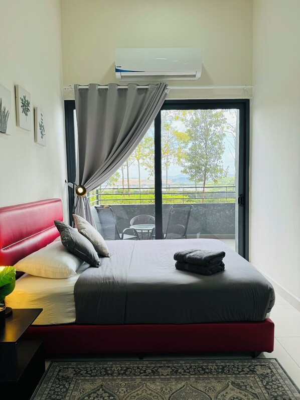 Un dormitorio con cabecera roja, ropa de cama gris, una mesita de noche negra y vistas a zonas verdes a través de un ventanal grande.