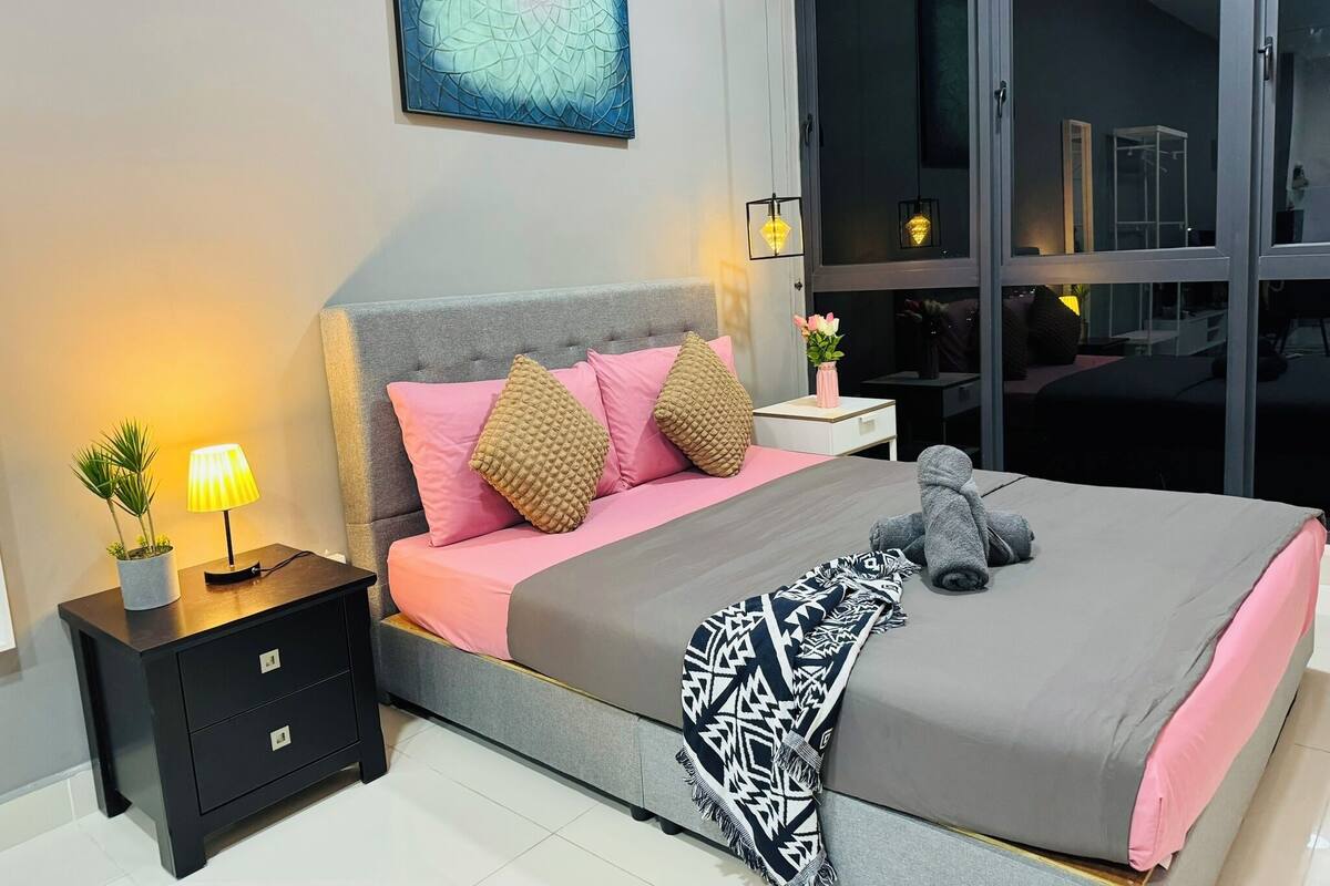 A modern bedroom with a grey headboard, pink bedding, and a large window.