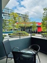 Uma varanda com vista para um edifício moderno, uma piscina e vegetação.