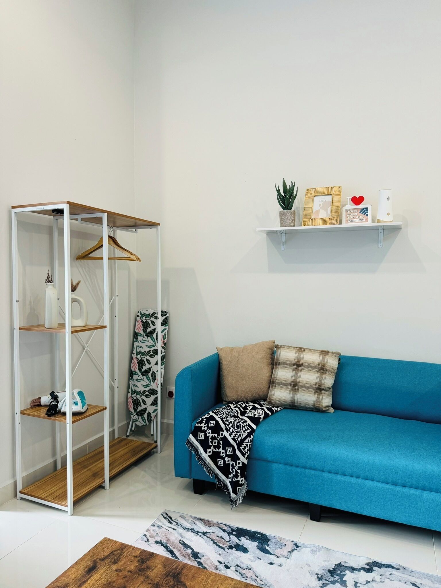Una habitación con un sofá azul, un perchero de madera, un estante blanco con adornos y una alfombra estampada.