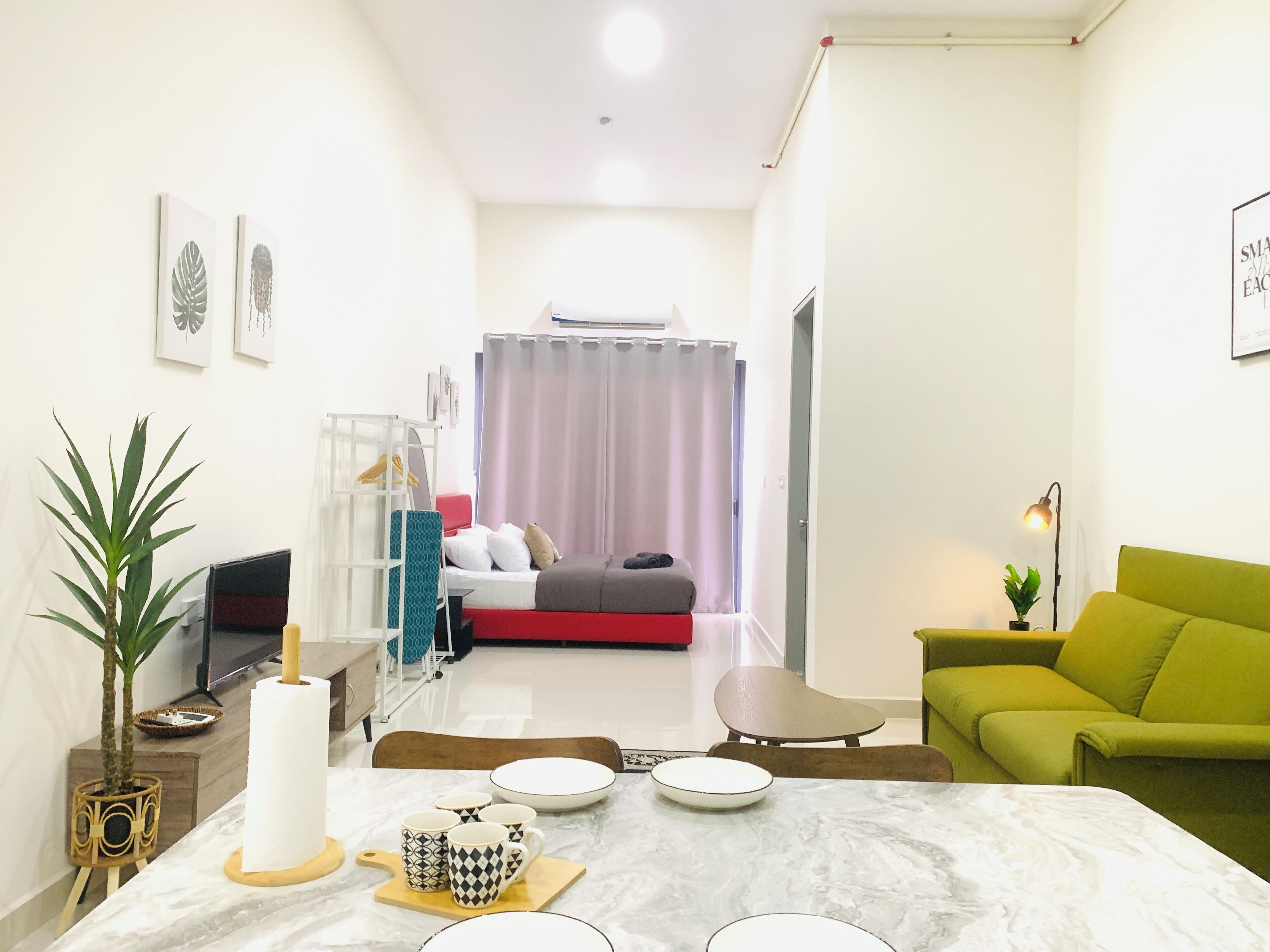 Una sala moderna con un sofá verde, una mesa de comedor con platos y tazas, un televisor y una cama con cabecera roja.