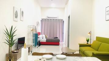 Un salon moderne avec un canapé vert, une table à manger avec des assiettes et des tasses, un téléviseur et un lit avec une tête de lit rouge.