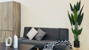 A modern living room with a grey sofa, a black coffee table, a wooden cabinet, and a large green plant.
